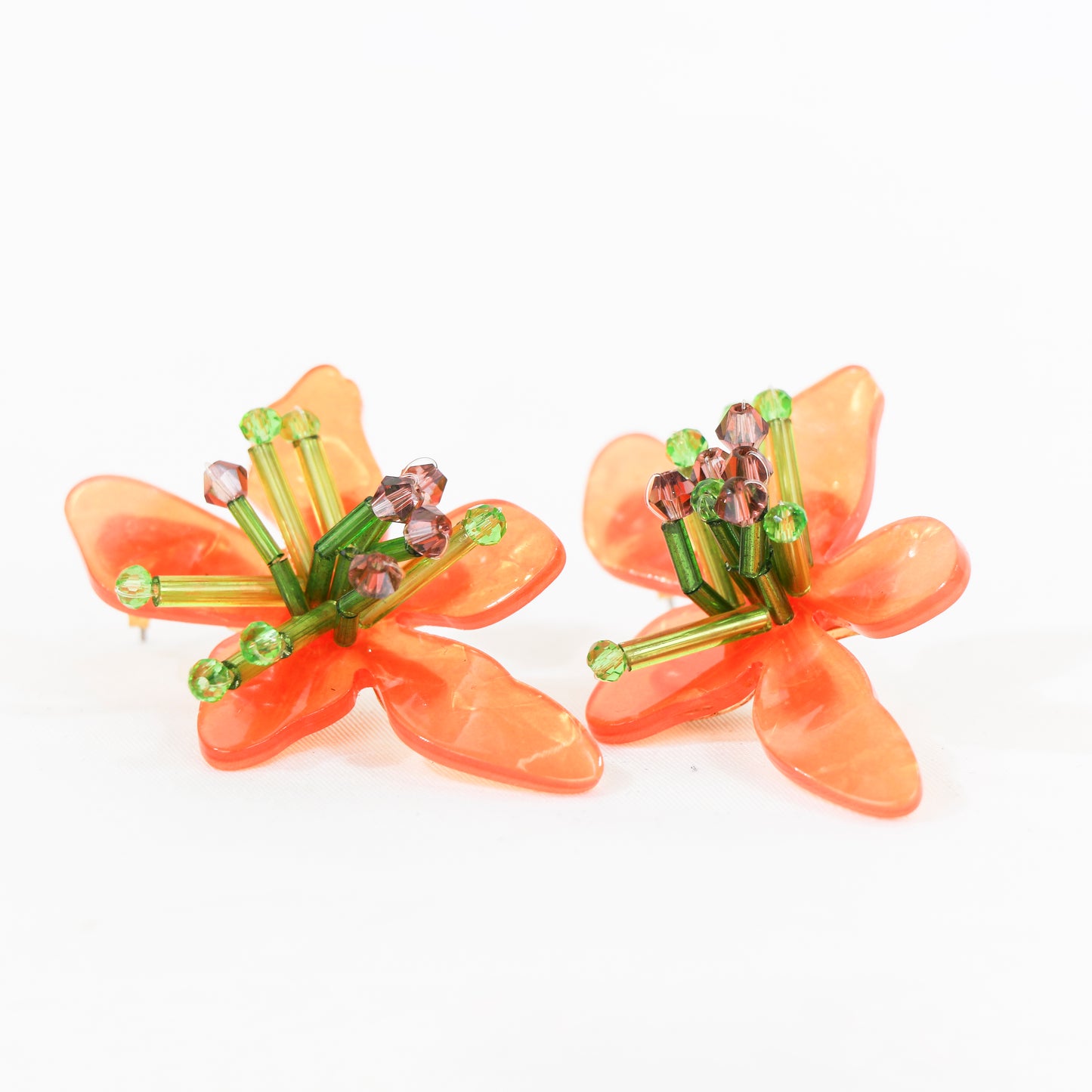 Pendientes coloridos en forma de flor de materiales acrílicos. Miden 55 mm de largo, y están disponibles en dos colores: naranja y verde, o lila y verde. El peso de cada pendiente es de 9 gr.