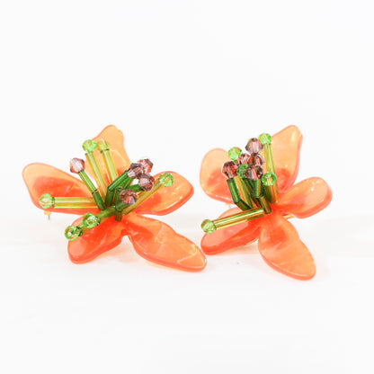 Pendientes coloridos en forma de flor de materiales acrílicos. Miden 55 mm de largo, y están disponibles en dos colores: naranja y verde, o lila y verde. El peso de cada pendiente es de 9 gr.